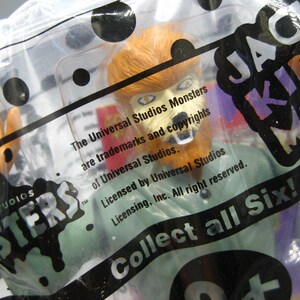 May include: A Universal Studios Monsters toy figure of a werewolf, packaged in a clear plastic bag. The figure has orange fur and a green shirt. Text on the packaging includes "Universal Studios Monsters" and "Collect all Six!"