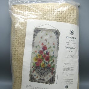 May include: A packaged rug kit with a floral design. The kit is in a clear plastic bag with a handle. The rug design features colorful flowers on a white background, with the text "gratulation" and "marks" visible.