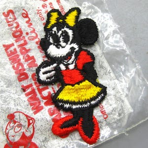 May include: Embroidered Minnie Mouse patch in black, red, yellow, and white. The patch is in a clear plastic package with red text that reads "WALT DISNEY APPLIQUES". The patch features Minnie Mouse in her classic outfit.