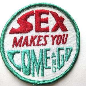 May include: Embroidered patch with the words "SEX MAKES YOU COME AND GO" in red and teal stitching. The text is on a white background, framed by a teal border. A humorous, novelty item.
