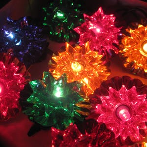 May include: A collection of multi-colored star-shaped light covers in shades of red, green, blue, orange, and pink. Each translucent plastic cover features a pointed, multi-faceted design that glows when illuminated by the internal light bulb.