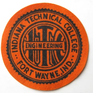 May include: Round orange felt coaster with black text. The text reads "INDIANA TECHNICAL COLLEGE FORT WAYNE, IND." around the edge, with "ENGINEERING" in the center. The coaster has a scalloped edge.