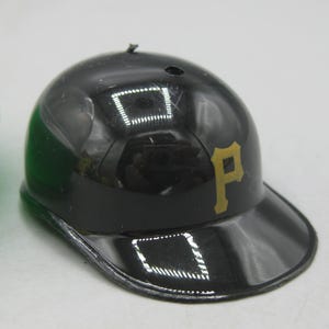 Op de afbeelding: Een zwarte honkbalhelm met een gouden "P" logo. De helm heeft een glanzende afwerking en een gebogen klep. Het is een miniatuur replica van een honkbalhelm.