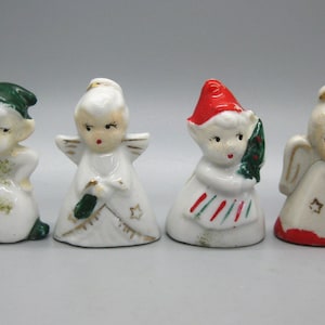 May include: A collection of four small ceramic Christmas figurines. The figurines depict an elf, an angel, a figure holding a Christmas tree, and an angel playing a harp. Each figurine is painted with white, red, green, and gold accents.