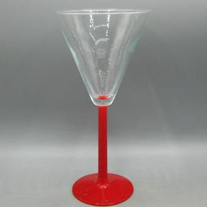 May include: A clear martini glass with a red stem and base. The glass has a classic triangular bowl shape and a long, slender stem. The base is round and provides stability. The glass is empty and ready for a cocktail.
