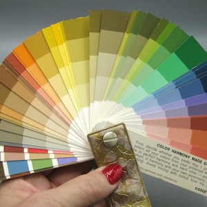 May include: A fan-shaped color swatch deck titled Color Harmony Made Easy, featuring a wide spectrum of paint color samples arranged in a circular layout. The deck is secured with a metallic fastener and displays various hues including yellow, orange, green, blue, and red tones, with printed instructional text on the bottom right corner.
