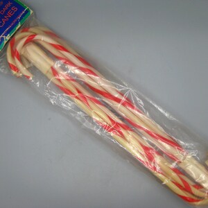 May include: A package of candy canes in a clear plastic bag. The candy canes are white with red stripes. The package has a blue and green label that reads "Glow-in-the-Dark Candy Canes".