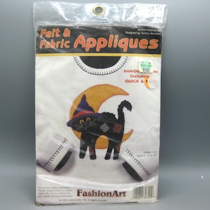 May include: A sealed packet of felt and fabric appliques. The design features a black cat wearing a witch's hat, sitting on a crescent moon. The package includes the text "Felt & Fabric Appliques" and "Iron-On". The image size is approximately 23 cm x 25 cm.