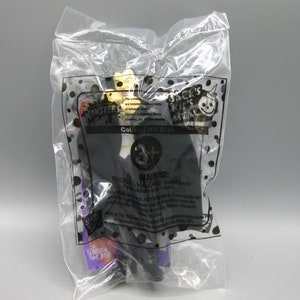 May include: A plastic bag containing a toy figure from Jack's Kids Meal. The figure is dressed in a black coat and has a light-colored face. The bag has the text "MONSTERS" and "Collect all Six!"