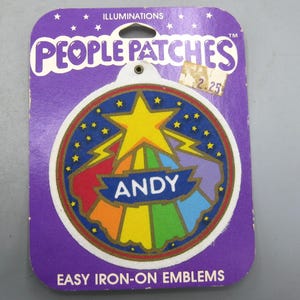 May include: A vintage People Patches iron-on emblem on a purple backing. The emblem features a star, lightning bolts, and a rainbow design with the name "ANDY" on a blue banner. The packaging reads "EASY IRON-ON EMBLEMS."
