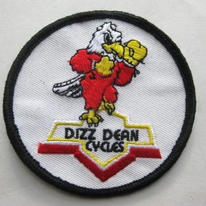 May include: Embroidered patch featuring a cartoon eagle in a red outfit and yellow boxing gloves. The eagle is on a white background with a black border. The text "Dizz Dean Cycles" is below the eagle.