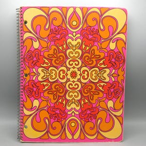 May include: A spiral-bound notebook featuring a vibrant, symmetrical pattern in shades of hot pink, bright orange, and yellow. The cover design consists of intricate, flowing organic shapes and curves that radiate from the center outward.