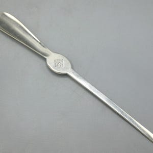 May include: A silver-toned nutcracker tool with a long, slender handle and a forked end. The handle has a rounded, oval-shaped center with a square design. The tool is designed for cracking nuts.