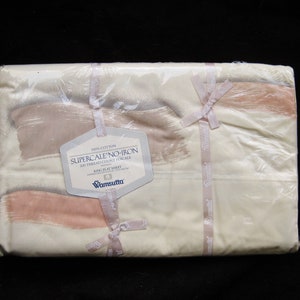 May include: A packaged king flat sheet by Wamsutta featuring a cream background with abstract brushstroke patterns in shades of tan and soft pink. The label reads 100% Cotton, Supercale No-Iron, 200 Thread Count Percale, and King Flat Sheet.