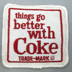 May include: Square white patch with red stitched border and text. The red text reads "things go better with Coke" with "TRADE-MARK ®" below. The patch has a white stitched border.