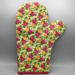 May include: A quilted oven mitt with a floral pattern of red and yellow roses on a light green background. The mitt has a red trim and is designed for kitchen use.