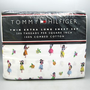 May include: A packaged Tommy Hilfiger twin extra long sheet set. The white sheets feature a repeating pattern of hula dancers in colorful skirts and floral accents. The packaging includes the brand name and product details.