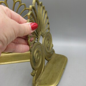 May include: A pair of antique brass bookends. Each bookend features an ornate, fan-shaped design with scroll details. The bookends are a warm, golden colour and appear to be made of solid brass. The base is approximately 10 cm long.