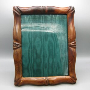 May include: A rectangular picture frame with a dark brown, polished wooden border featuring carved, scalloped edges and decorative corner accents. The center of the frame contains a textured, deep teal green insert with a vertical wavy pattern.