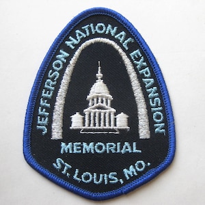 Puede incluir: Un parche azul y negro con el Jefferson National Expansion Memorial en St. Louis, MO. El parche tiene un borde azul e incluye el texto "JEFFERSON NATIONAL EXPANSION MEMORIAL ST. LOUIS, MO."