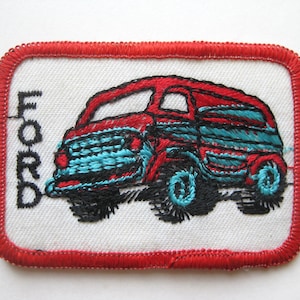 May include: Embroidered patch featuring a red and teal vintage Ford truck design. The patch has a white background with the word "FORD" embroidered vertically on the left side. The border is red.