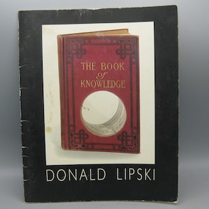May include: A book cover featuring a red book with the title "THE BOOK of KNOWLEDGE" in gold lettering. The book has a circular cutout revealing pages. The cover is set against a white background with a black border, and the author's name, DONALD LIPSKI, is at the bottom.