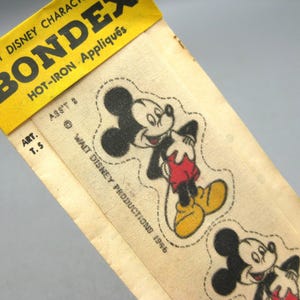 May include: A vintage Bondex hot-iron appliqué package featuring Mickey Mouse graphics on a cream-colored fabric strip. The yellow header displays the text Walt Disney Characters Bondex Hot-Iron Appliqués, Art. T. 5, Ass't 2, and Walt Disney Productions 1986.