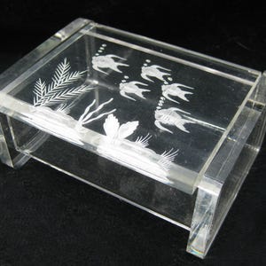 May include: A clear acrylic box with etched aquatic designs. The box features a rectangular shape with a lid and etched images of fish, seaweed, and plants. The box is transparent, allowing visibility of the contents.