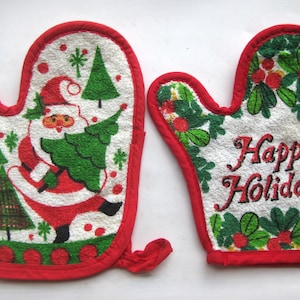 May include: A pair of white oven mitts with red trim. One mitt features a graphic of Santa Claus carrying a green Christmas tree among smaller trees. The other mitt displays green holly leaves with red berries and the text Happy Holidays in red.