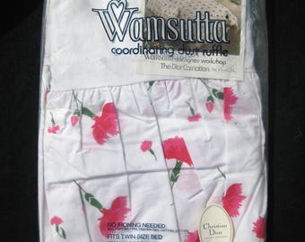 May include: A white twin-size bed dust ruffle in a plastic package. The ruffle features a floral pattern with pink flowers and green stems. The packaging includes the text "Wamsutta" and "Christian Dior".