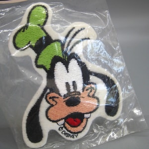 May include: A Disney Goofy patch in a clear plastic package. The patch features Goofy's face with a white background, black outline, green hat, and a red mouth. The Disney logo is at the bottom.