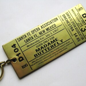 Op de afbeelding: Vintage messing ticket van de Santa Fe Opera Association, New Mexico, voor "Madame Butterfly", woensdag 3 juli 1957. Met stoelnummer D104. Het ticket is voor het orkest. De prijs was $4,80.