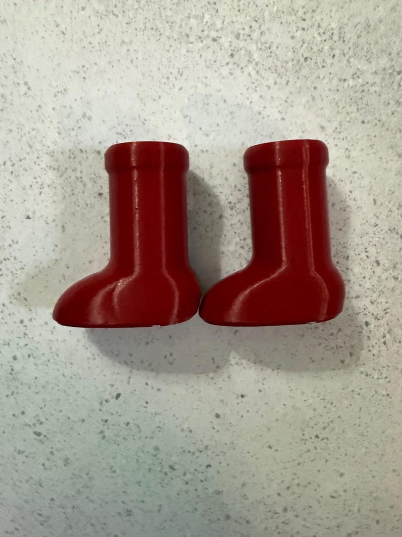 May include: Two small, bright red boots. The boots have a rounded toe and a cylindrical upper. The boots are likely decorative or for a small figurine. The boots are made of a solid material.
