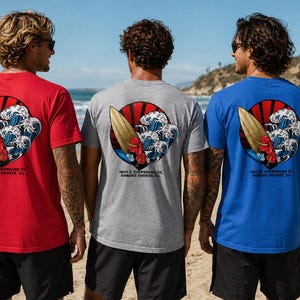 May include: Three t-shirts in red, gray, and blue, each featuring a surfboard graphic with waves and text. The shirts are short-sleeved and worn by people on a beach. A surfboard leans against a person.