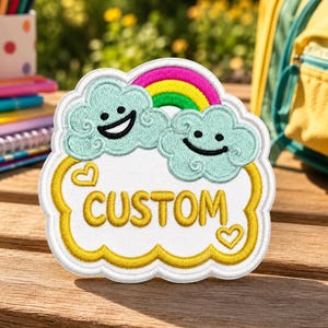 May include: A white embroidered patch featuring two light blue smiling clouds, a vibrant rainbow, and the word CUSTOM in yellow capital letters. The design includes two small yellow heart outlines and a thick yellow border on a white background.