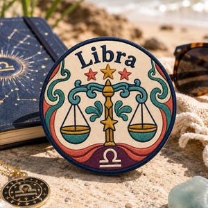 May include: A circular embroidered patch featuring the word Libra in dark blue text above a central scale icon. The design includes a gold central pillar, teal scale pans, red and gold stars, and a purple base with the Libra zodiac symbol in white.