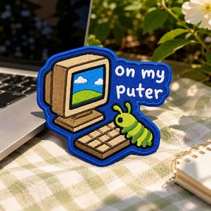 May include: An embroidered patch with a blue border featuring a beige vintage computer monitor displaying a blue sky and green hill landscape. A small green caterpillar sits on a brown keyboard. The white text reads on my puter.