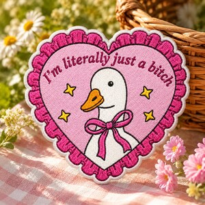 May include: A heart-shaped embroidered patch with a pink background and a dark pink ruffled border. It features a white goose with an orange beak wearing a pink bow, surrounded by four yellow stars and the text I'm literally just a bitch.
