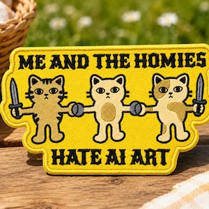 May include: A rectangular yellow embroidered patch featuring three cartoon cats holding hands. The cats on the ends hold daggers. The text reads ME AND THE HOMIES at the top and HATE AI ART at the bottom in bold black lettering with a stitched border.