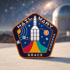 May include: A navy blue and orange embroidered patch with the words "HAIL MARY" and "GRACE" in white. The patch features a rocket ship launching with colorful flames and the name "ИЛЮХИНА" in white.
