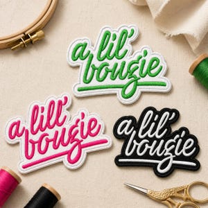 May include: Three embroidered patches featuring the text a lil' bougie in cursive script. One patch has green text on a white background, one has pink text on a white background, and one has white text on a black background with a white border.