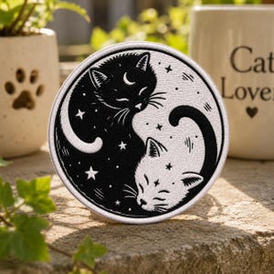 May include: A circular embroidered patch featuring a black and white yin-yang design composed of two curled cats. The black cat has a white crescent moon on its forehead, and the white cat has a small star on its forehead, surrounded by stars.