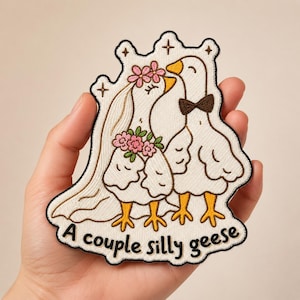 May include: Embroidered patch featuring a couple of geese, one wearing a bow tie and the other a veil and floral crown. The patch has the text "A couple silly geese" in a whimsical font, with a cream-colored background.