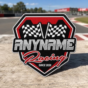 May include: A shield-shaped embroidered patch featuring a black background with red borders. It displays two checkered flags, the text ANYNAME in silver block letters, the word Racing in red script, and the text SINCE 2026 in white.