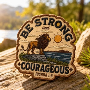 May include: Embroidered patch with a lion illustration and the text "BE STRONG and COURAGEOUS" with "Joshua 1:9" below. The patch features a lion standing on a rock, with a sun and clouds in the background. The patch has a brown border.