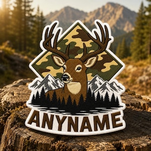 May include: A decorative patch featuring a brown deer with large antlers centered in front of a camouflage diamond shape. Below the deer are black silhouettes of pine trees and white mountain peaks. The word ANYNAME is printed in brown at the bottom.