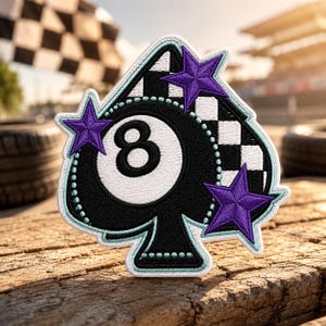 May include: An embroidered patch shaped like a spade playing card suit, featuring a central white eight ball, a black and white checkered pattern, and three purple stars. The design is outlined with a light blue border and white stitching.