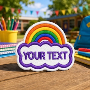 May include: An embroidered patch featuring a colorful rainbow arching over a white cloud shape with a purple border. The text "YOUR TEXT" is stitched in purple capital letters across the center of the white cloud section of the patch.