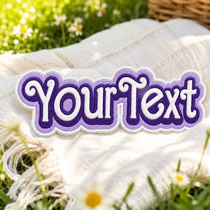 May include: A custom embroidered patch featuring the text YourText in a bold, stylized font. The lettering is white with a dark purple inner border and a light purple outer border, creating a layered effect with a scalloped edge outline.