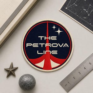 May include: A circular patch with the text "THE PETROVA LINE" in white, set against a navy blue background. The design includes a red and white graphic and two white stars. The patch is surrounded by a cream-colored border.